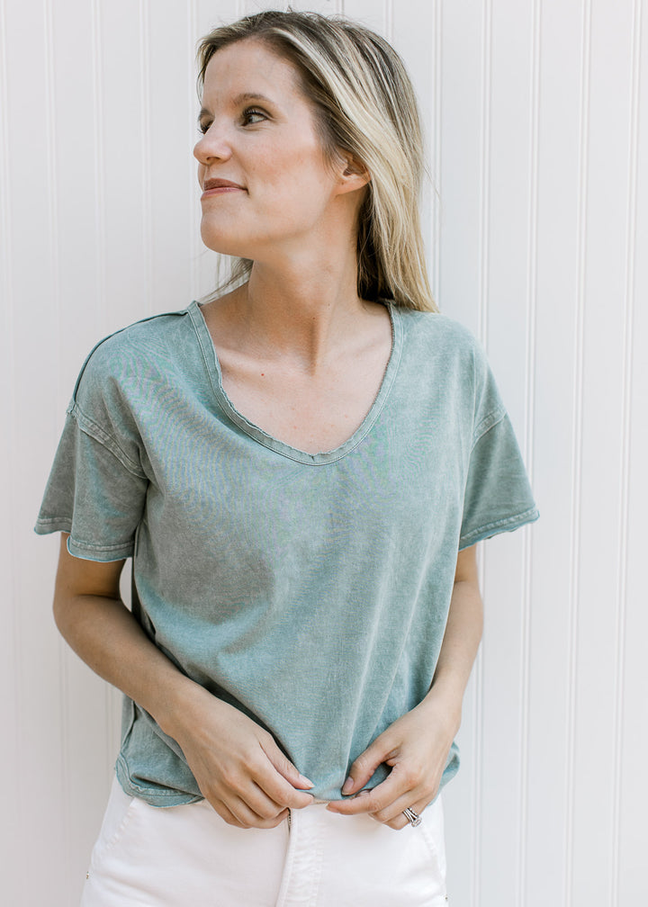 Model wearing a slate blue top with a v- neck, short sleeves and a raw hemline.
