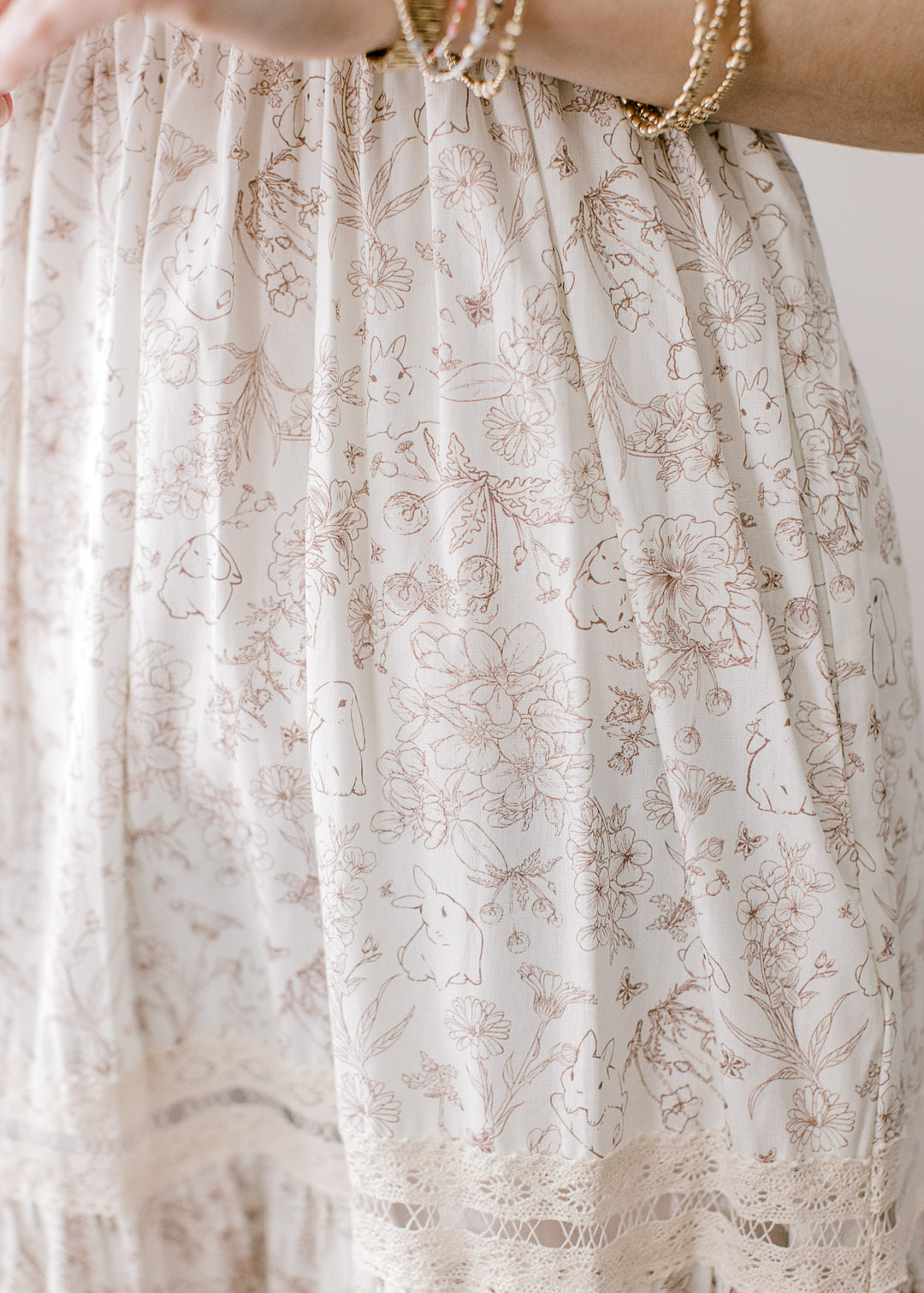 Close up of light brown bunnies and floral on a cream maxi with a smocked bodice and lace straps.
