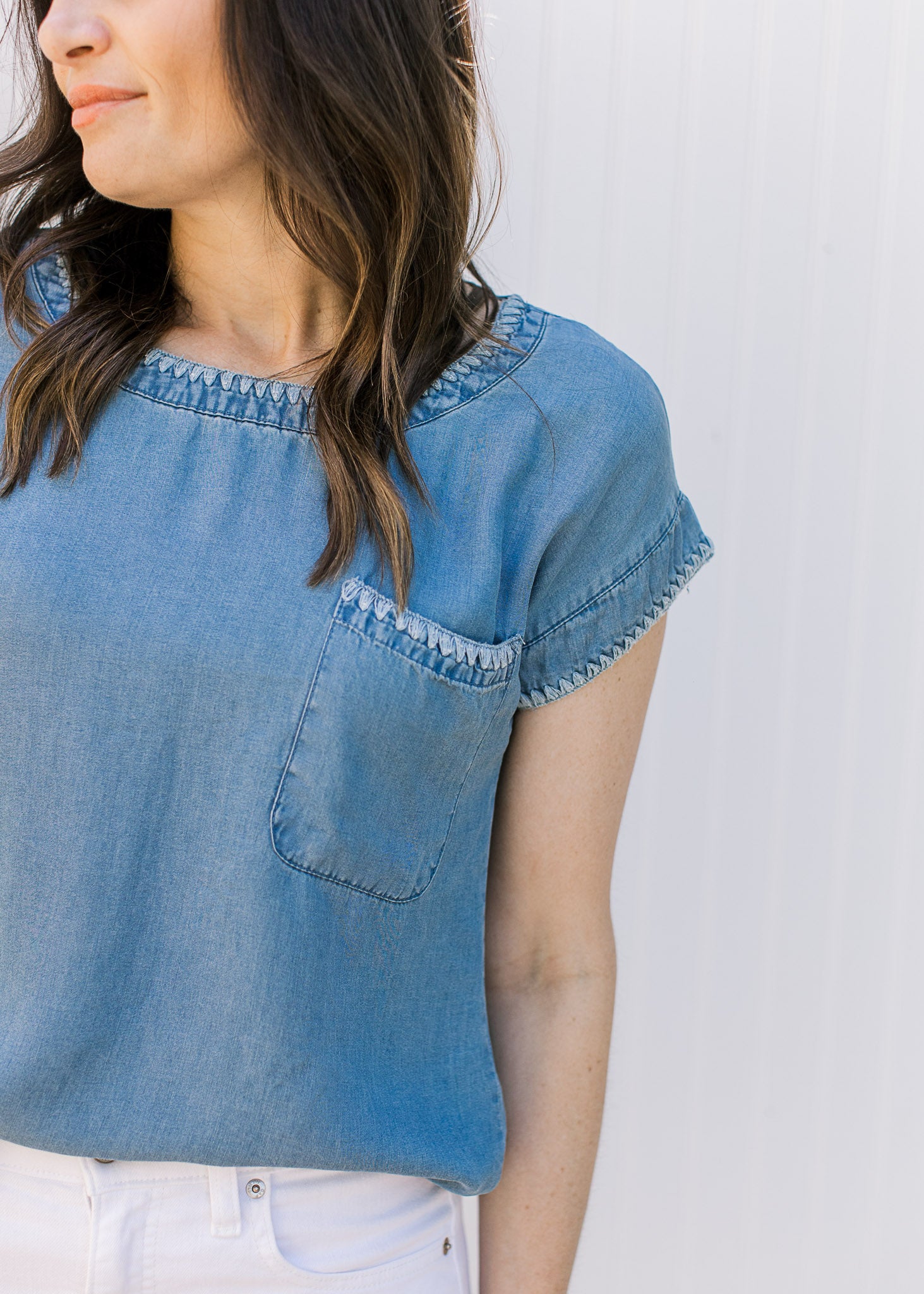 Close up of detail stitching at the neck, cuff and patch pocket on a chambray top. 