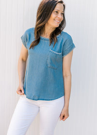 Model wearing white pants and a chambray top with capped sleeves and stitching detail. 