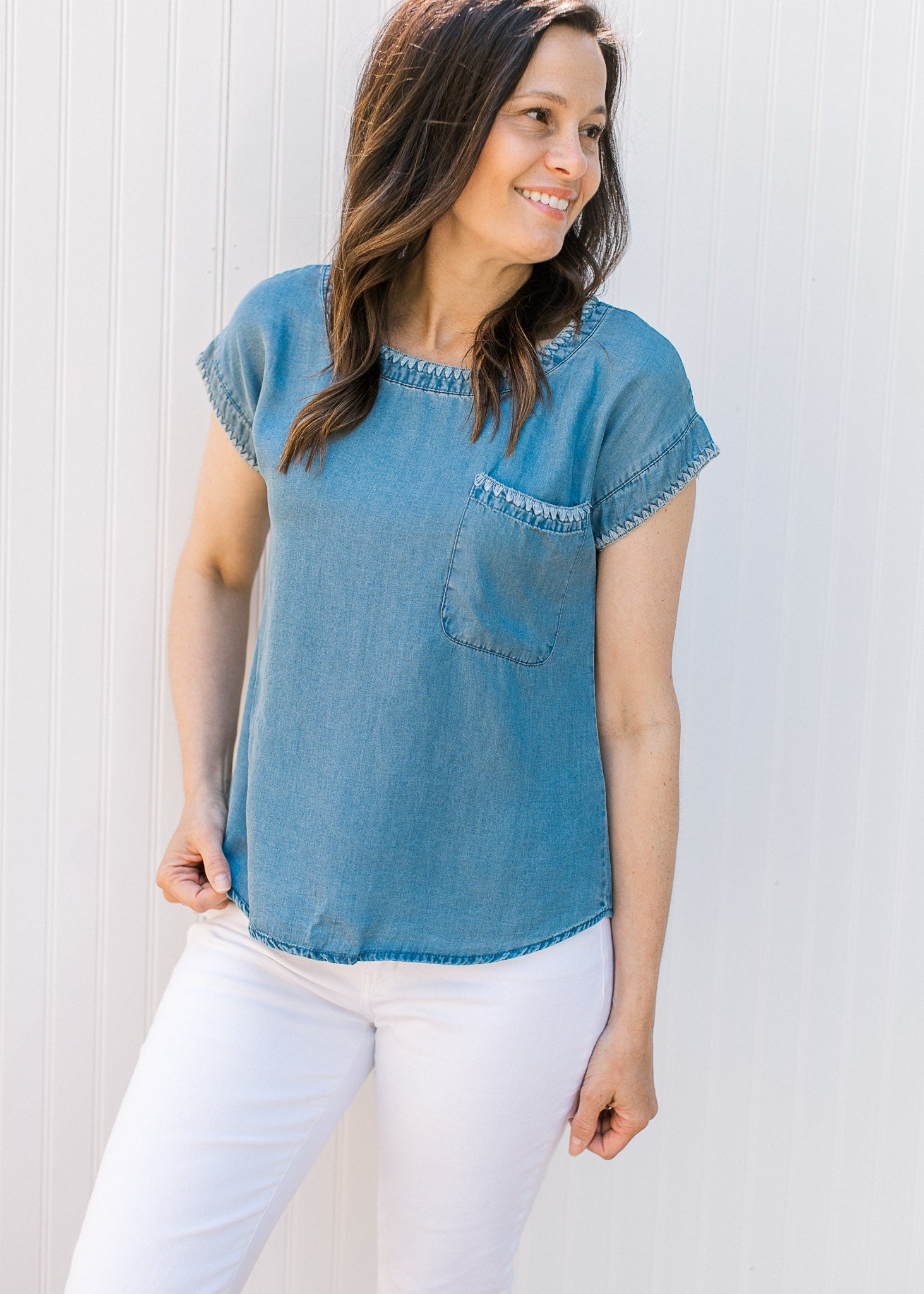 Model wearing white pants and a chambray top with capped sleeves and stitching detail. 