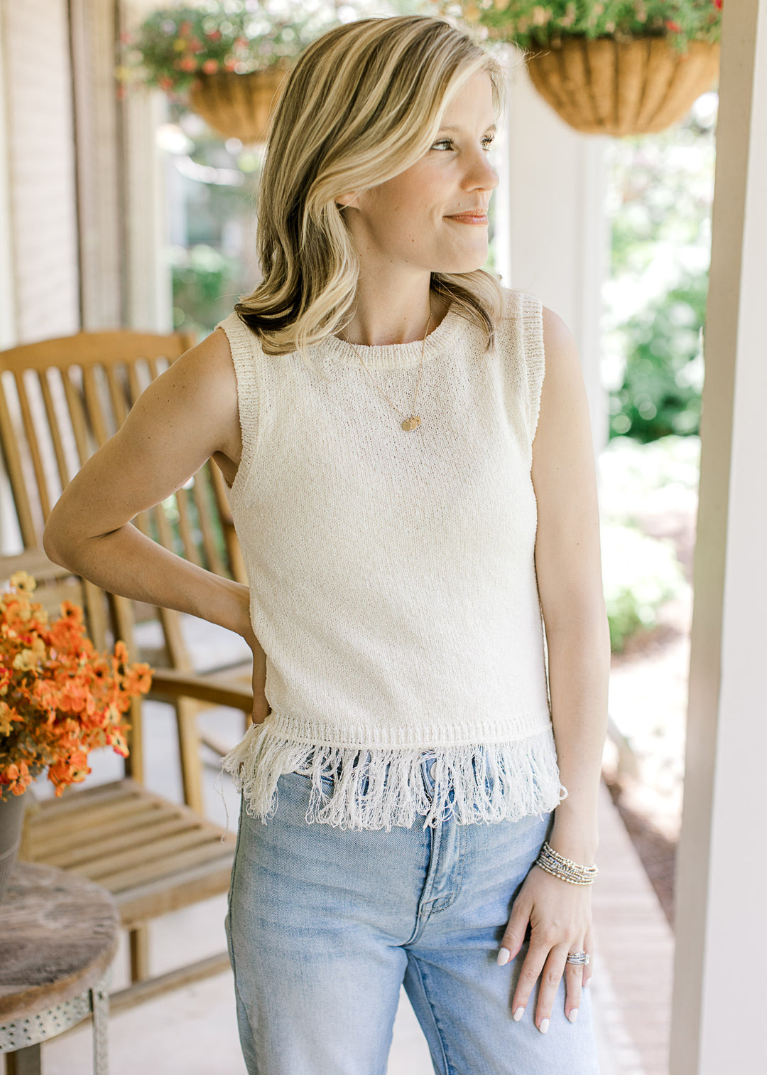 Model wearing a cream sleeveless blouse with a round neck, fringe hem detail and a lightweight knit.
