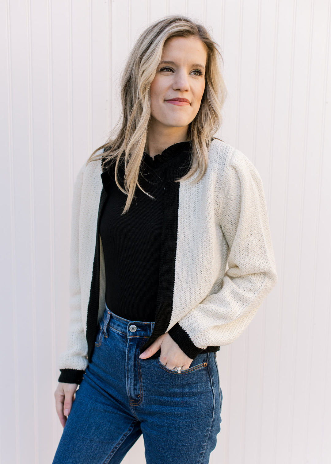 Model wearing a cream open front sweater with a black cuff, hem and neckand a classic fit. 