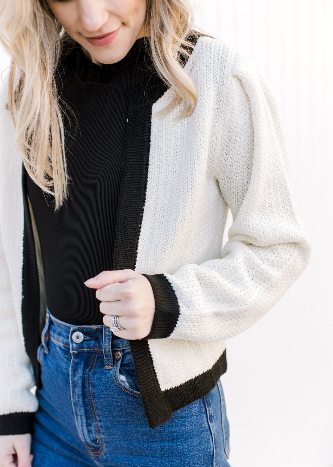Close up of black on cuff, neck and hem of a cream cardigan with an open front. 
