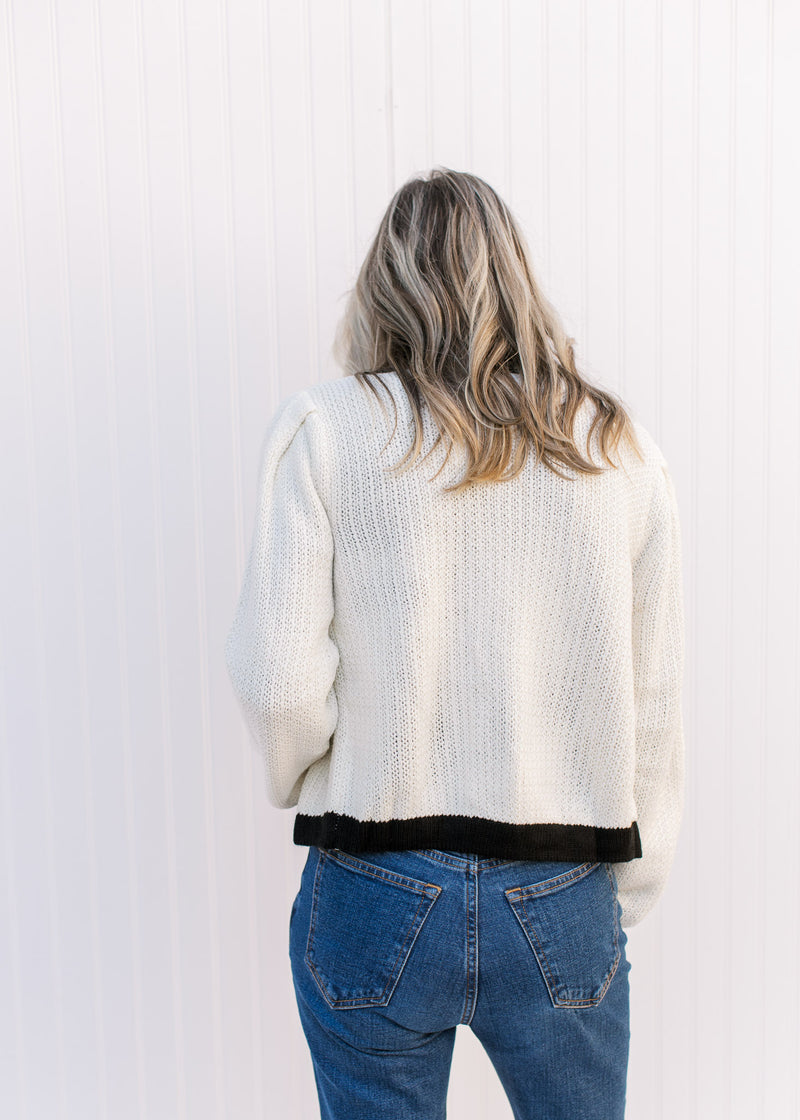 Back view of Model wearing a cream sweater with a black cuff, hem and neck, with a classic fit.
