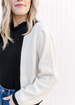 Close up of the sleeve on a cream cardigan with black hem, neck and sleeve.