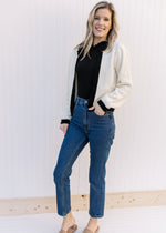 Model wearing jeans, a black top and mules with a cream sweater with a classic fit.