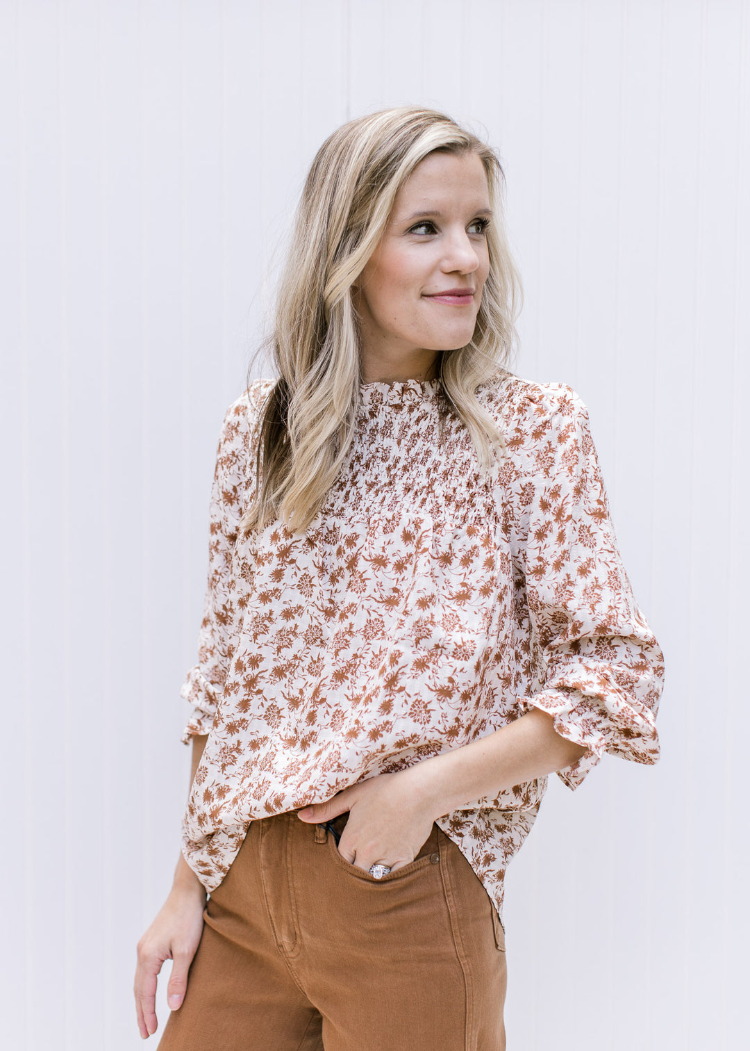 Model wearing cream top with brown floral, a smocked yolk, 3/4 poet sleeves and ruffled round neck.