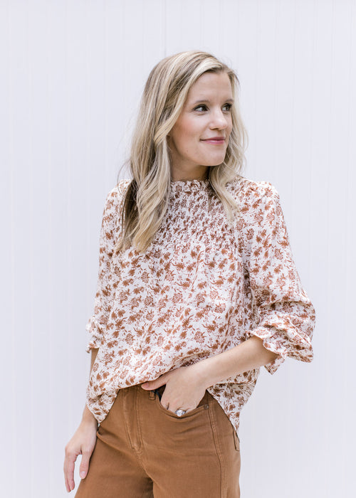 Model wearing cream top with brown floral, a smocked yolk, 3/4 poet sleeves and ruffled round neck.