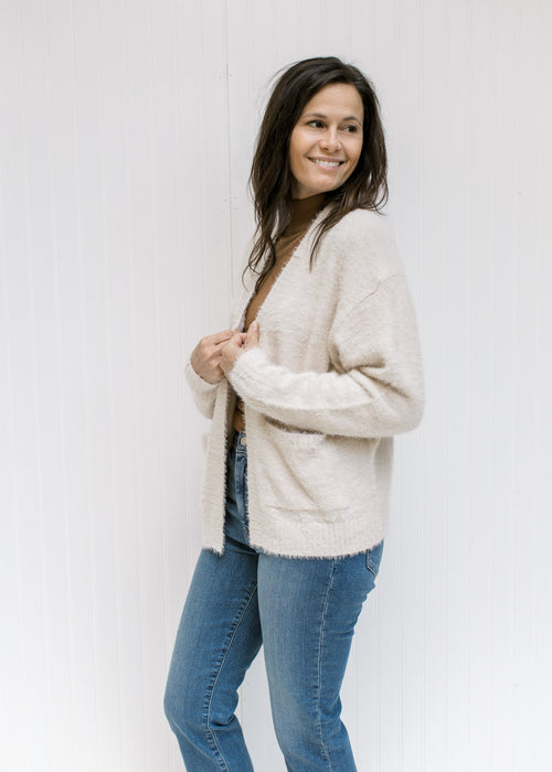 Model wearing a beige open front, long sleeve cardigan with a ribbed detail at hem and cuff. 
