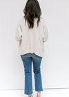 Back view of Model wearing a beige open front, long sleeve cardigan with a ribbed hem and cuff. 