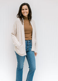 Model wearing a camel top with jeans and a beige open front cardigan with long sleeves. 