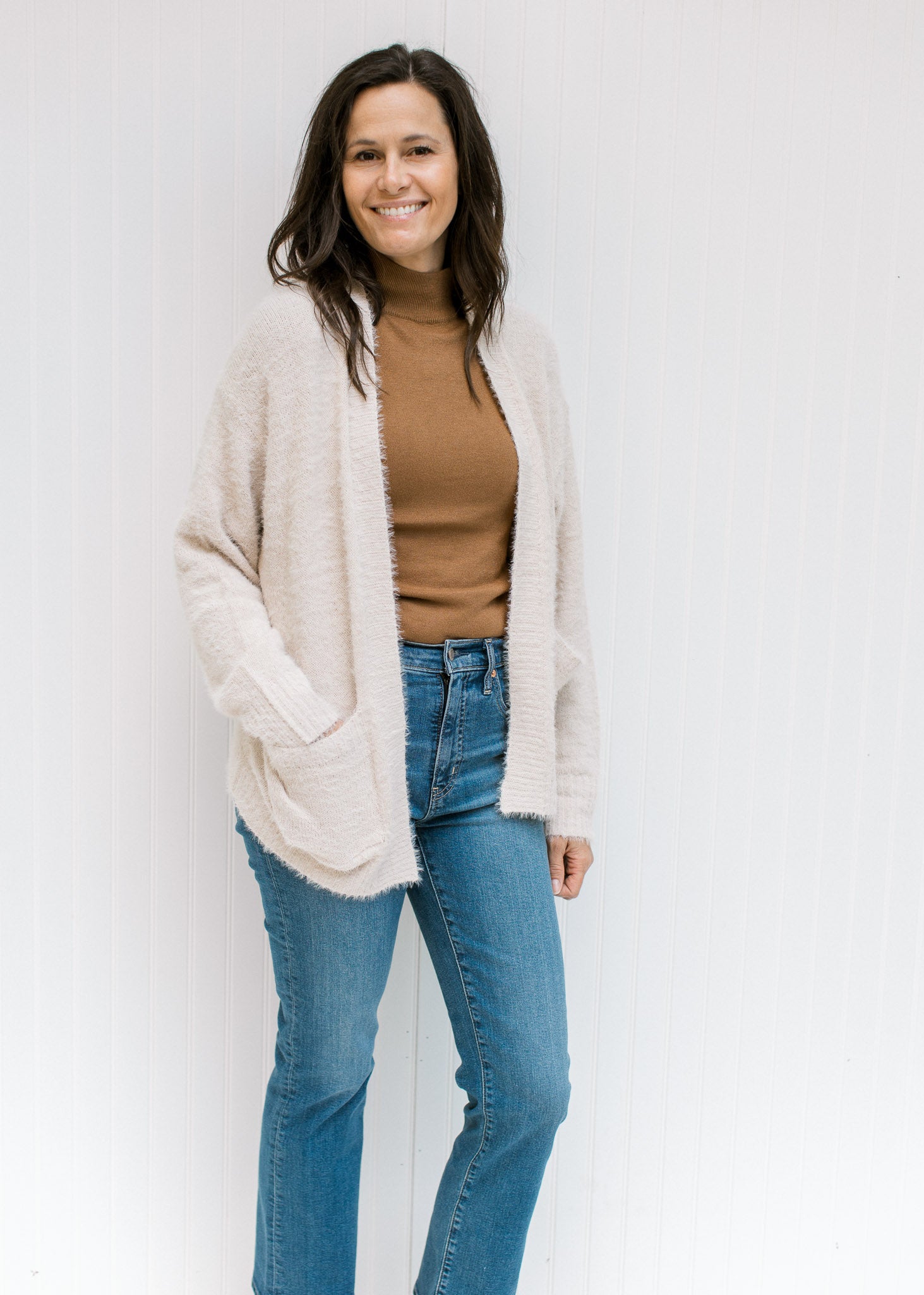 Model wearing a camel top with jeans and a beige open front cardigan with long sleeves. 