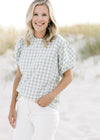 Model wearing a sage and white plaid top with smocked shoulder and neck detail and short puff sleeve