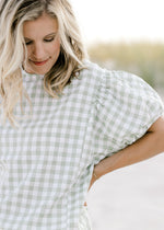 Close up of smocked detail at shoulder and neck on a sage and white plaid top with short sleeves. 