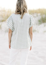Back view of model wearing a sage and white plaid top with a button up closure. 
