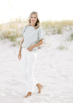 Model wearing white jeans with a sage and white plaid top with short puff sleeves.