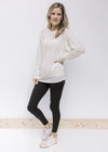 Model wearing black leggings and sneakers with a cream long sleeve top with a round neck. 
