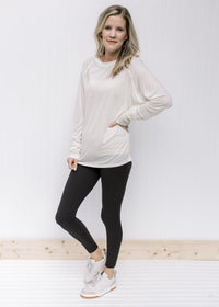 Model wearing black leggings and sneakers with a cream long sleeve top with a round neck. 