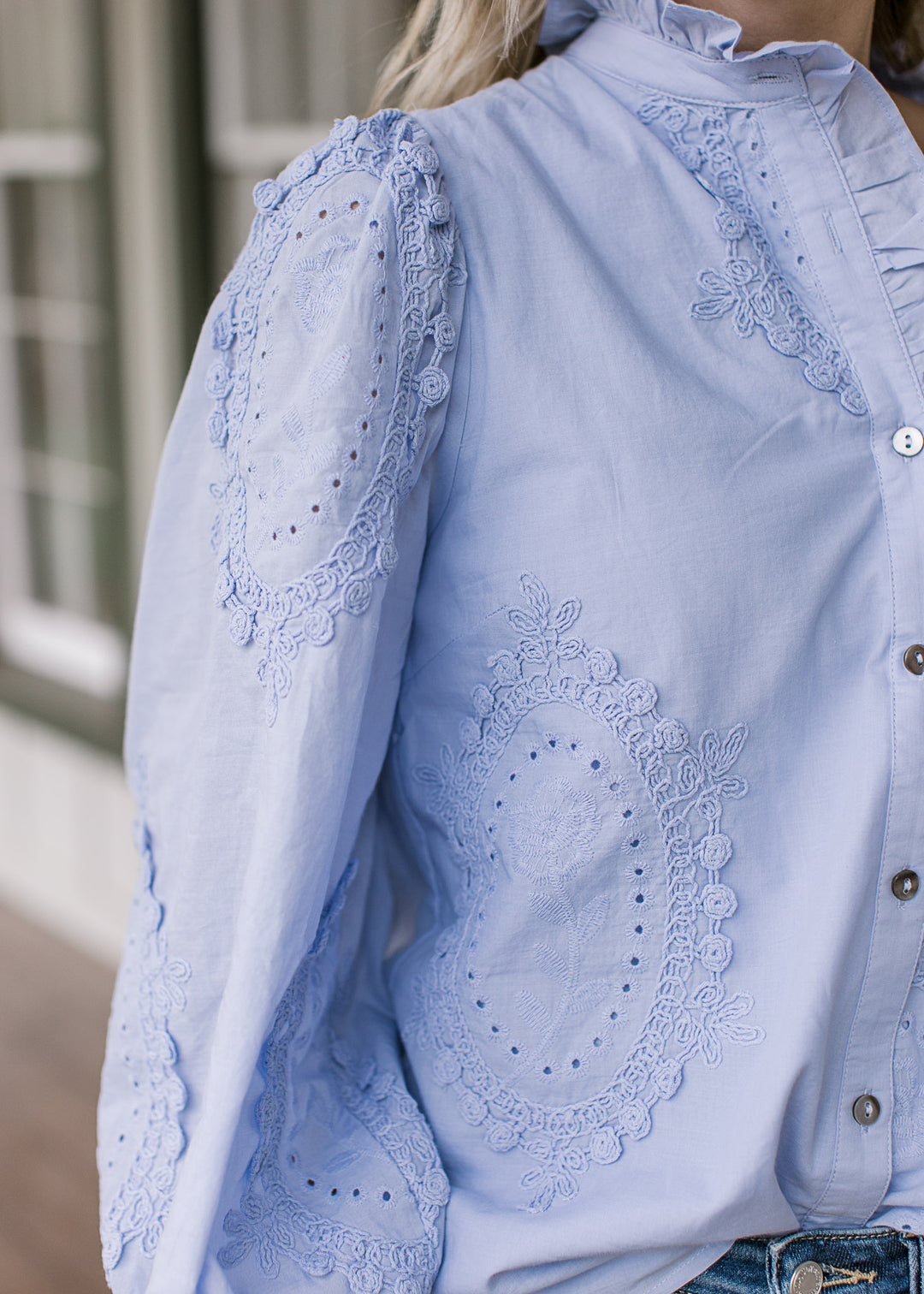 Close up of tone-on-tone floral medallions and ruffle detail at neck of a soft blue long sleeve top.