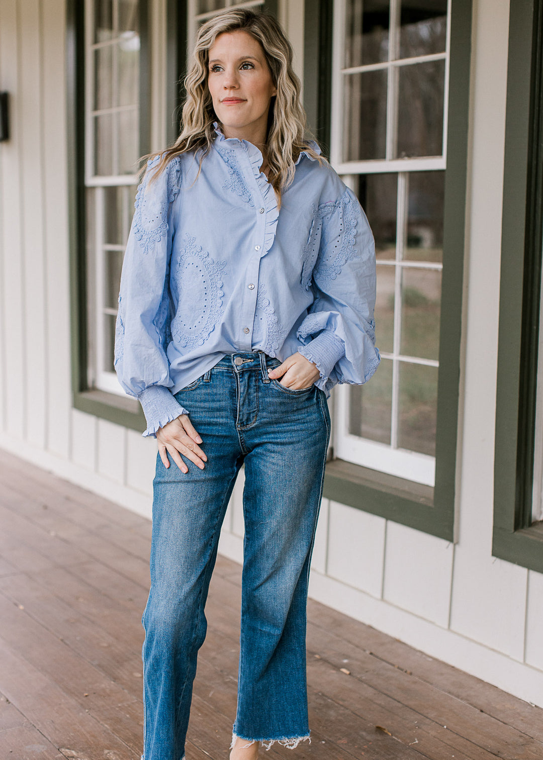 Model wearing a soft blue top with tone-on-tone floral medallions and ruffle detail at the neck.