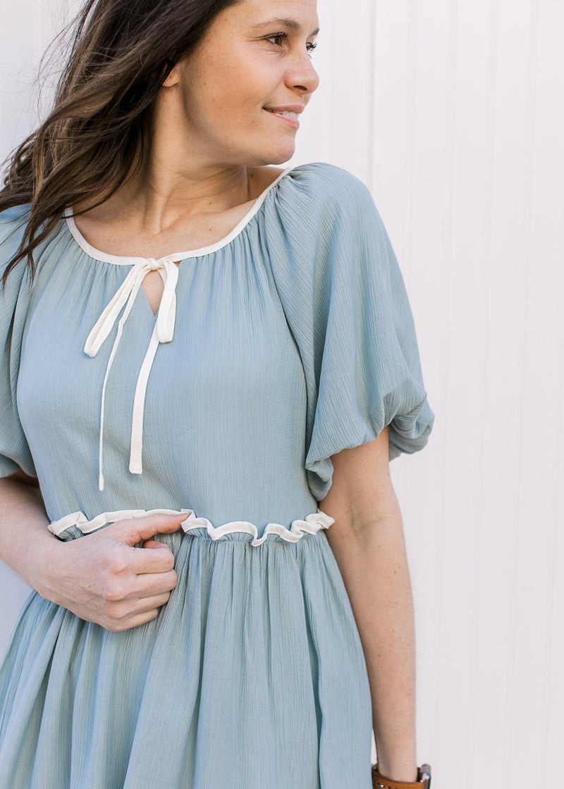 Close up of keyhole tie at neck, cream piping and bubble short sleeves on a pale blue-green dress.