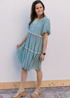 Model wearing sandals and a pale blue-green dress with cream piping and tie keyhole at neck.