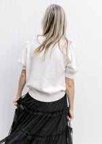 Back view of Model wearing a cream v-neck sweater with 2 black shimmer bows and short sleeves. 