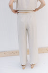 Back view of Model wearing oatmeal colored linen pants with wide legs and a tie closure.