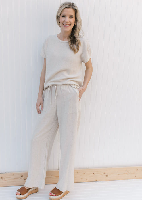 Model wearing oatmeal colored linen pants with front patch pockets, wide legs and a tie closure.