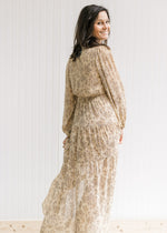 Back view of model wearing a tan maxi with a sheer overlay, elastic wasit and sheer long sleeves. 