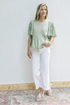 Model wearing white pants and wedges with a soft green top, pleated front and tie detail on sleeves.