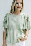 Model wearing a soft green top with pleated front and tie detail on the short sleeves. 