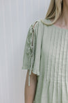 Close up of tie closure on short sleeve of a soft green top with pleated front. 