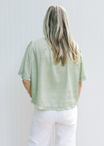 Back view of Model wearing a soft green top with pleated front and tie detail on the short sleeves.