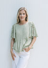 Model wearing a soft green top with ruffle at cuff and hem and tie detail on the short sleeves.