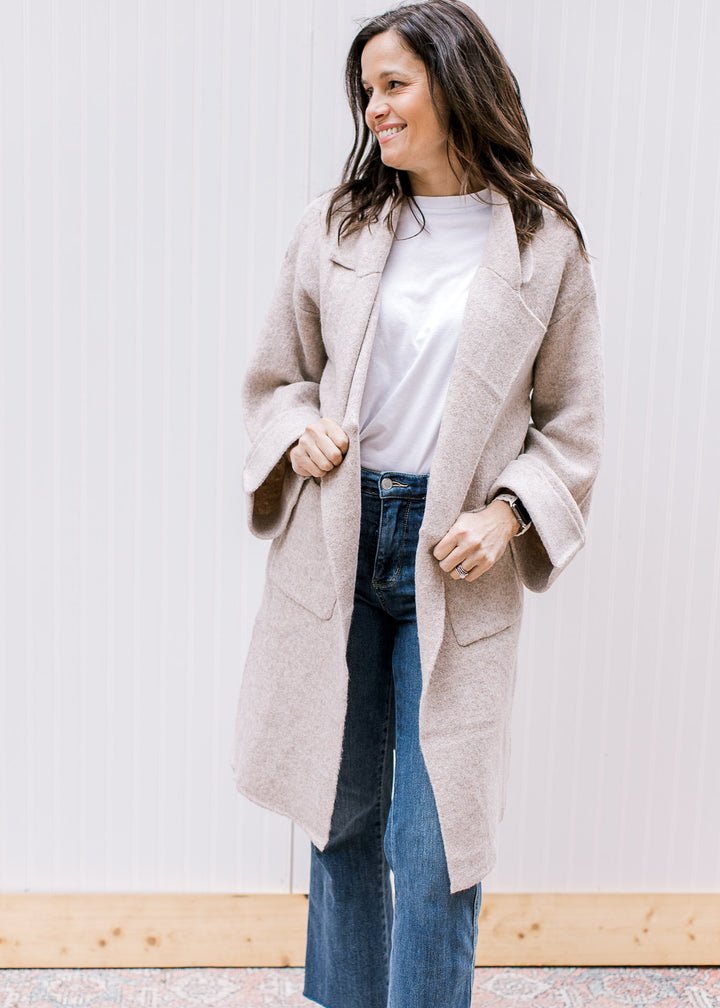 Model wearing an oatmeal open front cardigan with a flap collar and long sleeves with a cuff. 