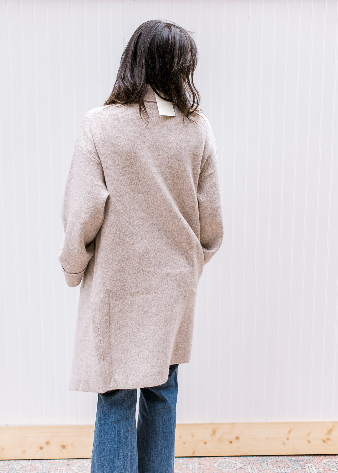 Back view of Model wearing an oatmeal open front cardigan with a flap collar and long sleeves. 