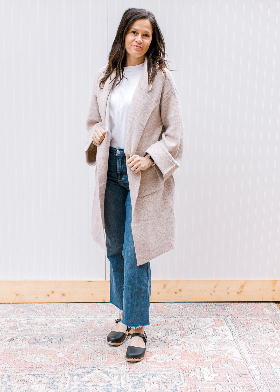 Model wearing jeans and an oatmeal cardigan with a flap collar and long sleeves with a cuff. 