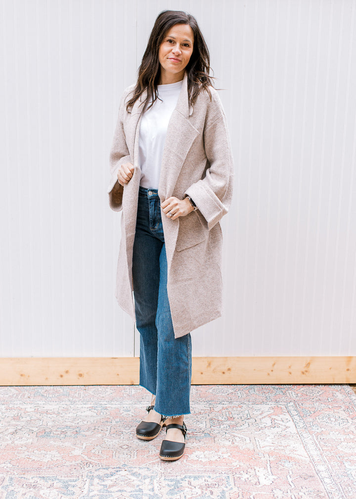 Model wearing jeans and an oatmeal cardigan with a flap collar and long sleeves with a cuff. 