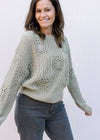 Model wearing a soft olive sweater with crochet flowers, long sleeves and a round neck. 