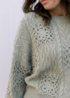 Come up of crochet flowers on a soft olive colored sweater with long sleeves and a round neck. 