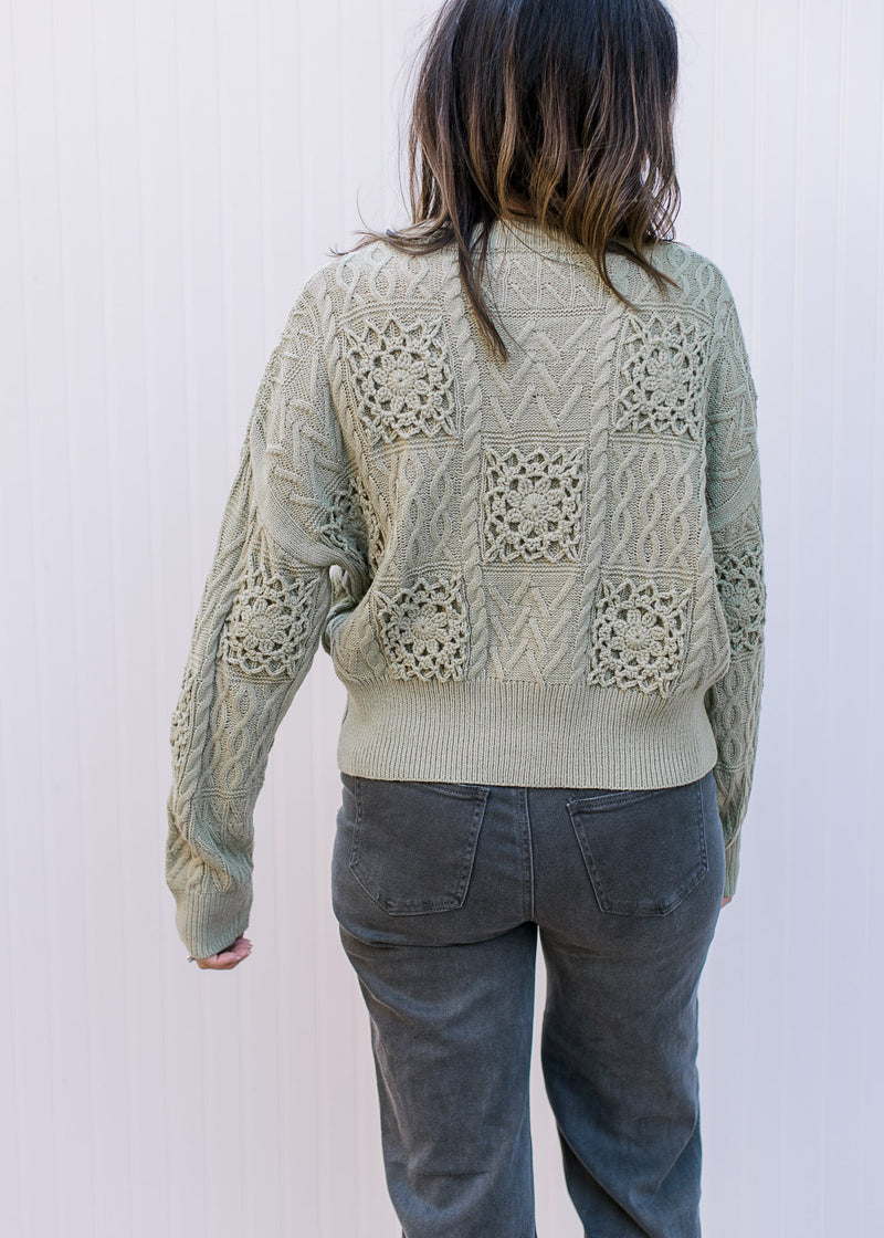 Back view of Model wearing a soft olive sweater with crochet flowers, long sleeves and round neck. 