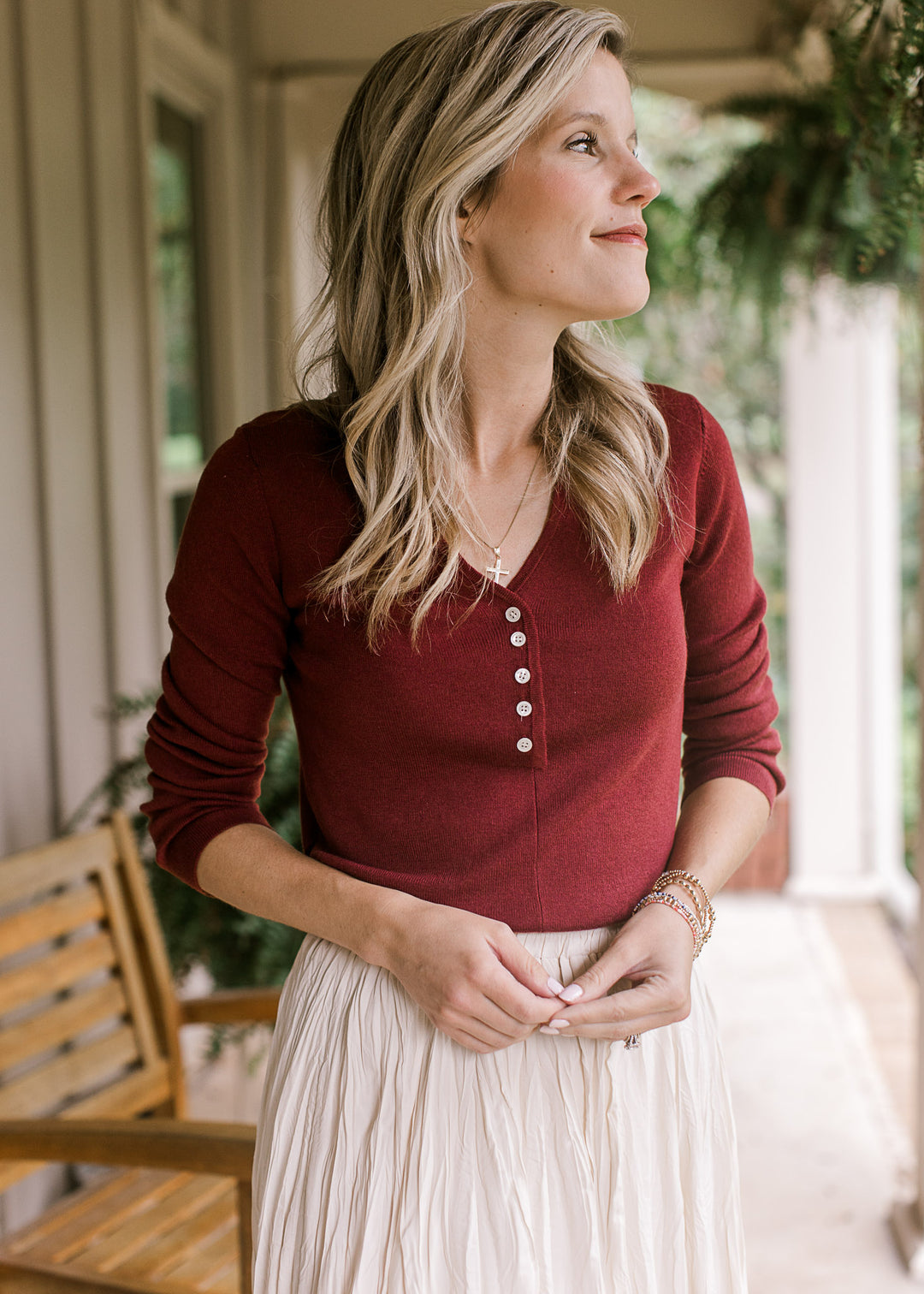 Model wearing a deep burgundy top with a v-neck with five working buttons and long sleeves. 
