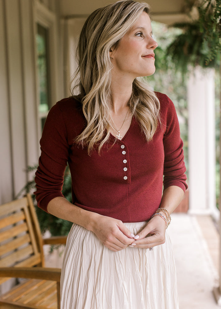 Model wearing a deep burgundy top with a v-neck with five working buttons and long sleeves. 