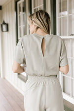 Close up of single button closure and short sleeves on a sage jumpsuit with an elastic waist. 