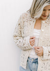 Model wearing a taupe floral crochet cardigan with a button front and long sleeves. 