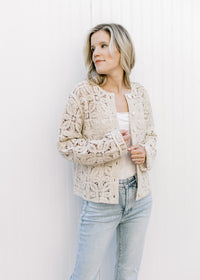 Model wearing a cream top and a taupe floral crochet cardigan with a button front and long sleeves. 
