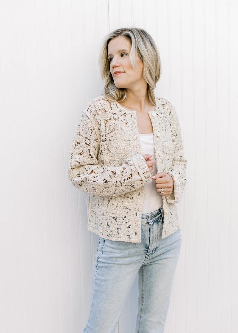 Model wearing a cream top and a taupe floral crochet cardigan with a button front and long sleeves. 