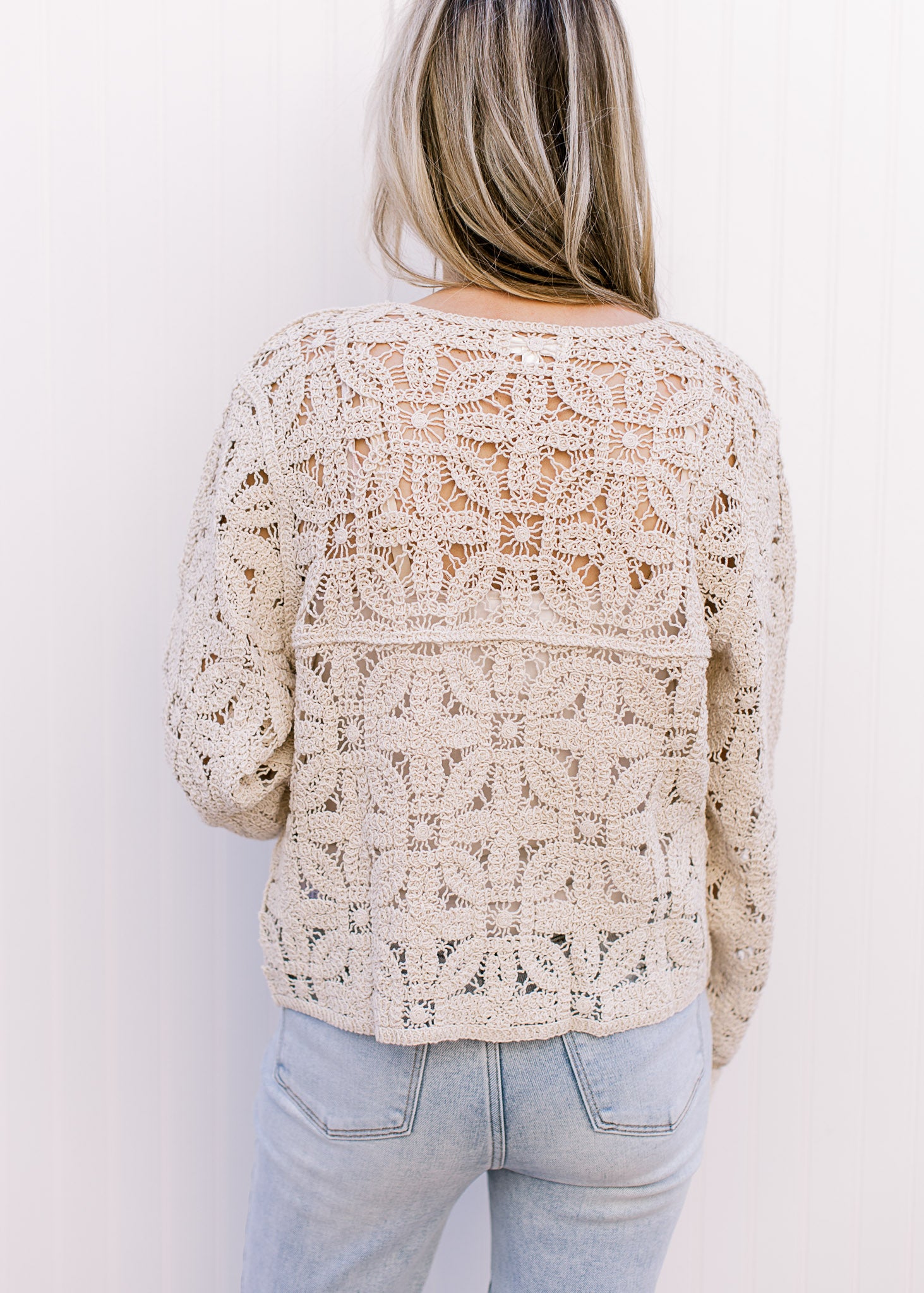 Back view of Model wearing a taupe floral crochet cardigan with a button front and long sleeves. 